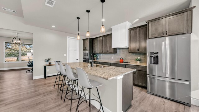 kitchen with premium range hood, light stone countertops, light wood-type flooring, dark brown cabinetry, and stainless steel appliances