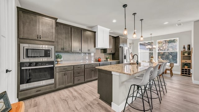 kitchen featuring light stone countertops, stainless steel appliances, light hardwood / wood-style flooring, pendant lighting, and a center island with sink