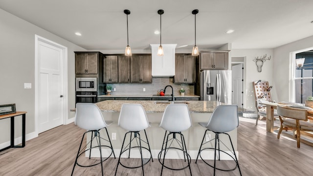 kitchen with pendant lighting, sink, light hardwood / wood-style flooring, light stone countertops, and appliances with stainless steel finishes