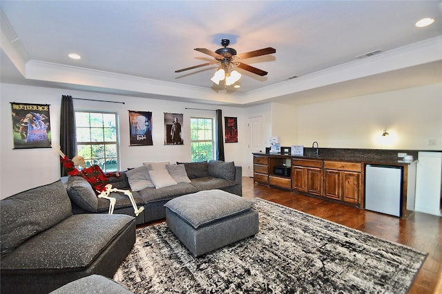 living room with a raised ceiling, ceiling fan, a wealth of natural light, and dark wood-type flooring