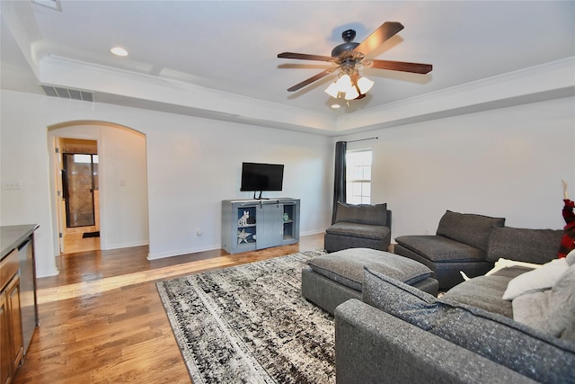 living room featuring wood-type flooring, ceiling fan, a tray ceiling, and ornamental molding