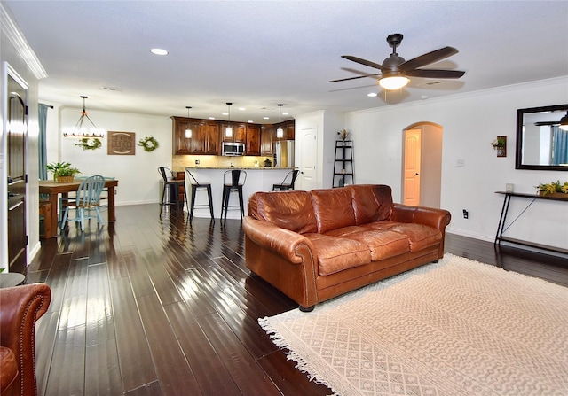 living room featuring ceiling fan with notable chandelier, ornamental molding, and dark hardwood / wood-style floors