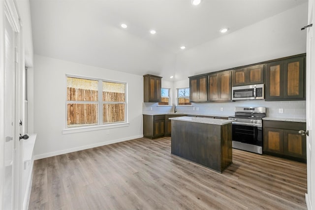 kitchen with lofted ceiling, appliances with stainless steel finishes, backsplash, and a center island