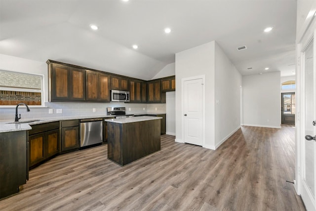 kitchen with appliances with stainless steel finishes, a center island, a sink, and dark brown cabinetry