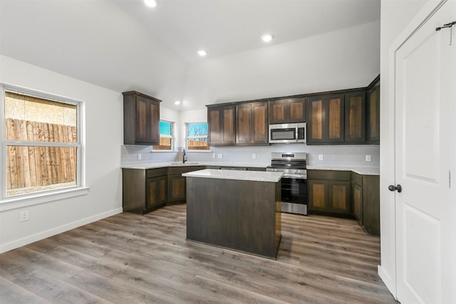 kitchen with lofted ceiling, appliances with stainless steel finishes, a sink, light countertops, and backsplash