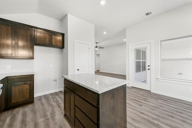 kitchen with visible vents, lofted ceiling, a kitchen island, dark brown cabinets, and light wood-style floors