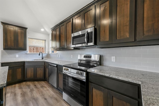 kitchen featuring dark brown cabinetry, appliances with stainless steel finishes, a sink, vaulted ceiling, and backsplash