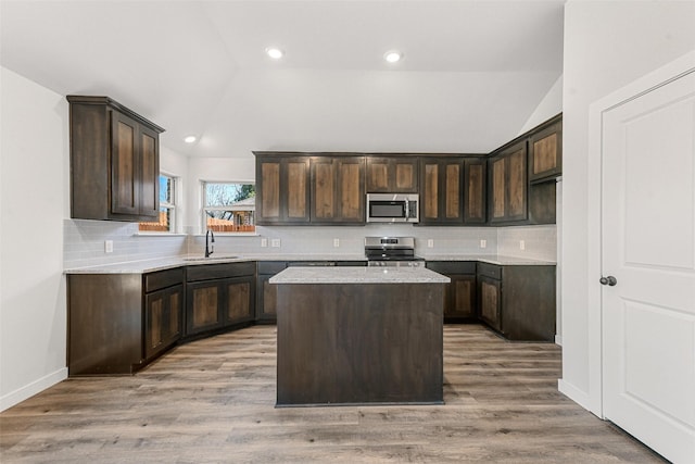 kitchen with dark brown cabinetry, lofted ceiling, stainless steel appliances, light wood-type flooring, and a sink