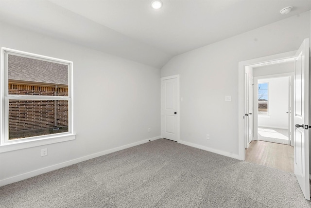 empty room with light colored carpet, vaulted ceiling, and baseboards