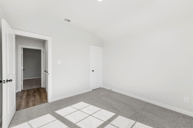 empty room with lofted ceiling, carpet flooring, visible vents, and baseboards