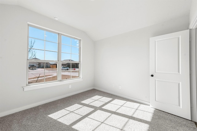 carpeted spare room featuring lofted ceiling and baseboards