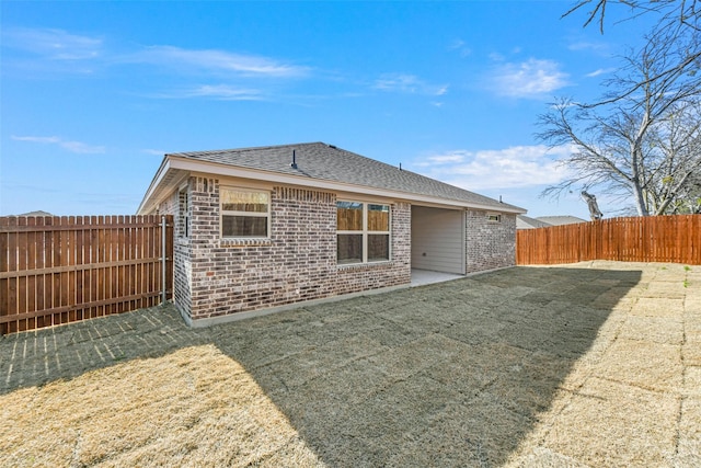 rear view of property featuring brick siding, a yard, roof with shingles, a patio area, and a fenced backyard