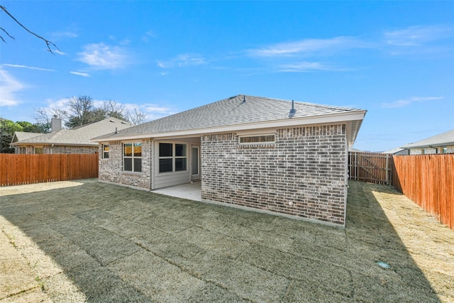 back of property featuring roof with shingles, brick siding, a patio, a lawn, and a fenced backyard