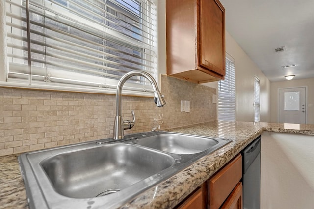 kitchen featuring tasteful backsplash, stainless steel dishwasher, sink, and light stone counters