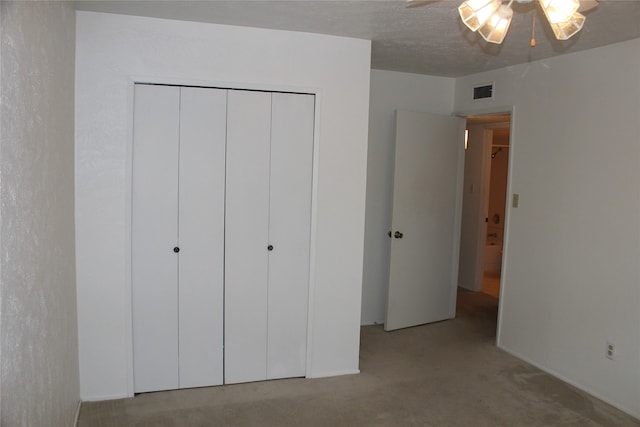 unfurnished bedroom featuring ceiling fan, a closet, light colored carpet, and a textured ceiling