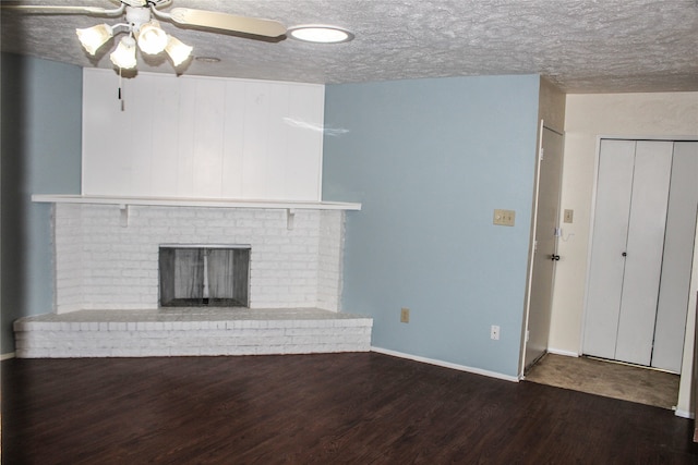 unfurnished living room featuring a textured ceiling, ceiling fan, dark wood-type flooring, and a brick fireplace