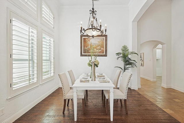 dining area with ornamental molding, dark wood-type flooring, and an inviting chandelier