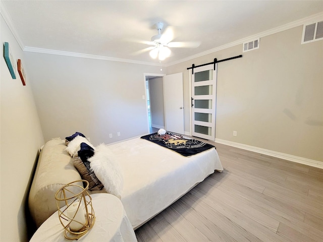 bedroom with ceiling fan, a barn door, light wood-type flooring, and crown molding