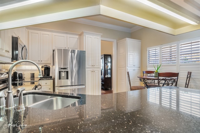 kitchen with sink, dark stone countertops, white cabinets, ornamental molding, and stainless steel appliances