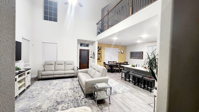 living room with ceiling fan with notable chandelier, light hardwood / wood-style floors, and a high ceiling