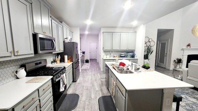 kitchen with sink, tasteful backsplash, light hardwood / wood-style floors, gray cabinets, and appliances with stainless steel finishes