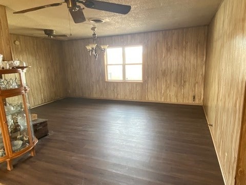 unfurnished room with a textured ceiling, dark hardwood / wood-style floors, ceiling fan with notable chandelier, and wooden walls