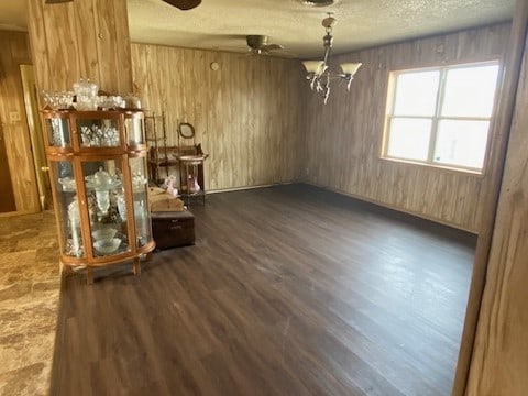 unfurnished dining area with a textured ceiling, ceiling fan with notable chandelier, dark wood-type flooring, and wood walls