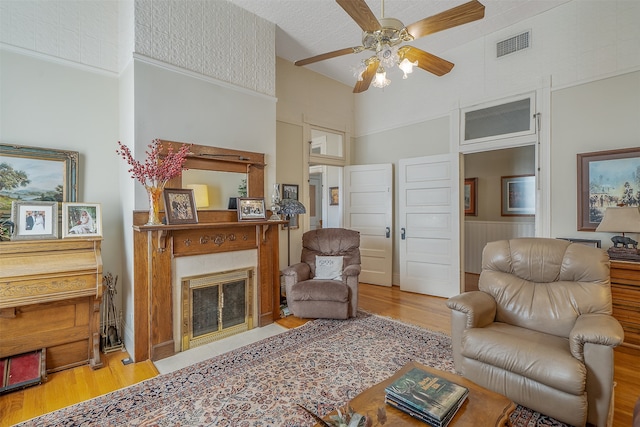 living room featuring a high ceiling, a tiled fireplace, ceiling fan, and wood-type flooring