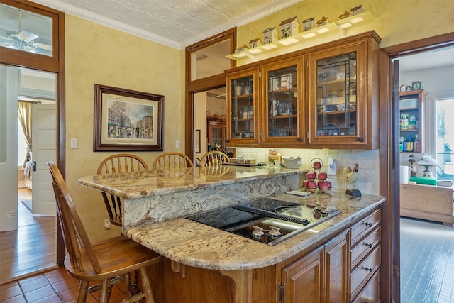 kitchen with a breakfast bar, dark wood-type flooring, black electric stovetop, light stone countertops, and ornamental molding