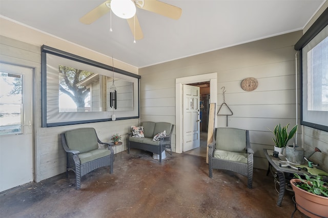 living area featuring wooden walls, ceiling fan, and a wealth of natural light