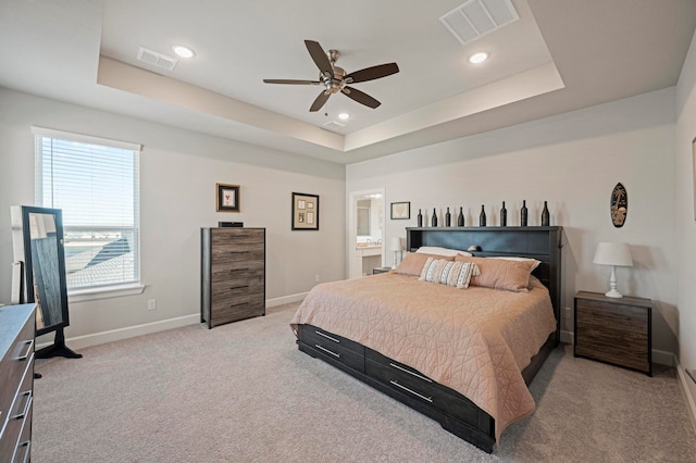 carpeted bedroom featuring a raised ceiling, ensuite bath, and ceiling fan