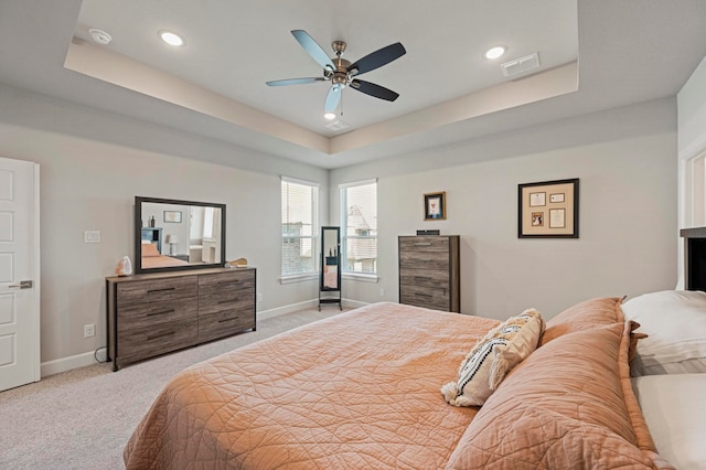 bedroom with light colored carpet, ceiling fan, and a tray ceiling