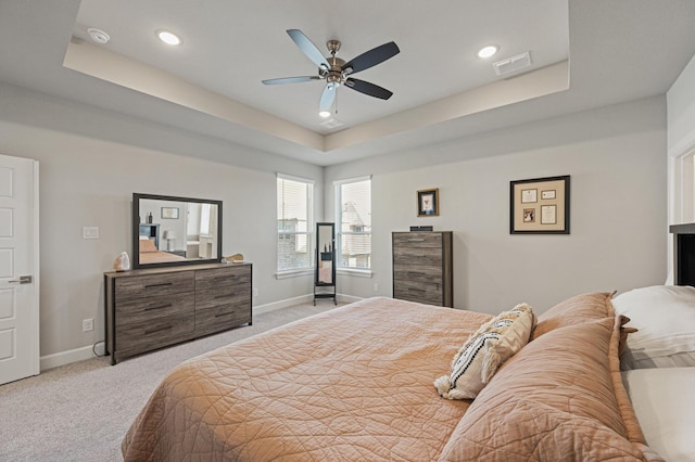 bedroom featuring a raised ceiling, light colored carpet, and ceiling fan