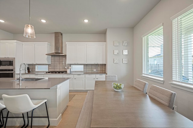 kitchen with sink, wall chimney exhaust hood, stainless steel appliances, tasteful backsplash, and pendant lighting