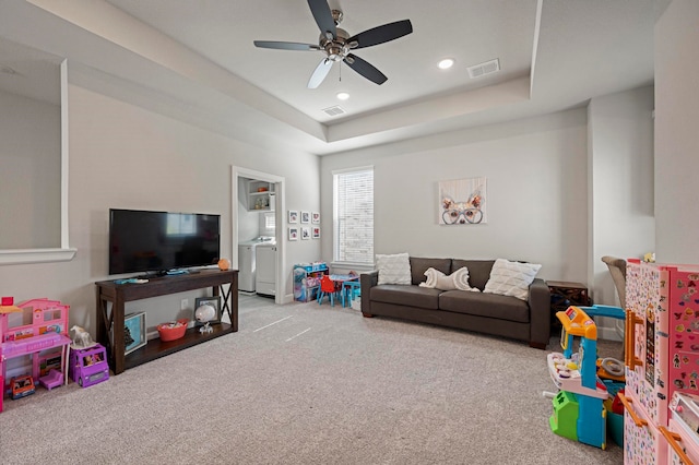 recreation room featuring a raised ceiling, ceiling fan, washing machine and dryer, and light carpet