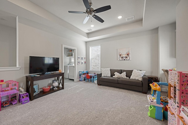 game room featuring light carpet, ceiling fan, washer and dryer, and a raised ceiling