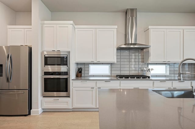 kitchen featuring white cabinets, wall chimney range hood, sink, decorative backsplash, and appliances with stainless steel finishes