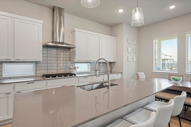 kitchen with wall chimney range hood, hanging light fixtures, sink, white cabinetry, and stainless steel gas cooktop