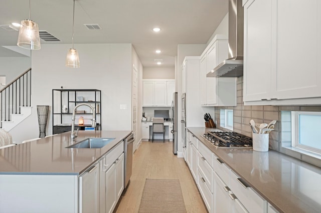 kitchen with pendant lighting, wall chimney range hood, sink, light wood-type flooring, and stainless steel appliances