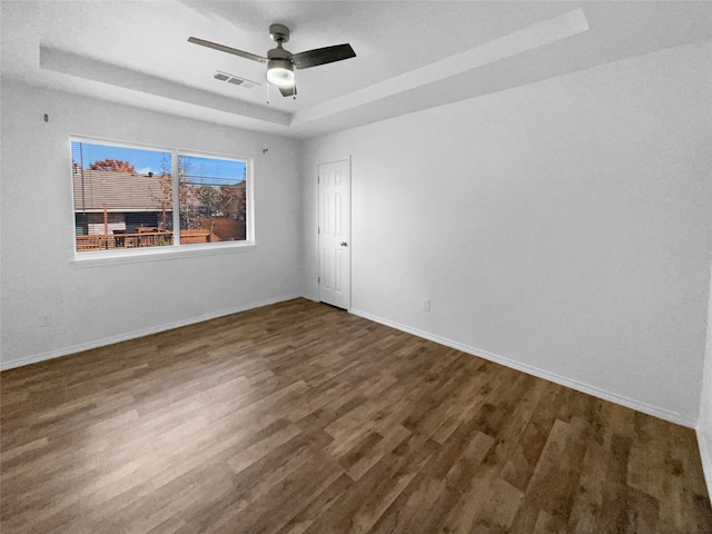 empty room with dark hardwood / wood-style flooring and a tray ceiling