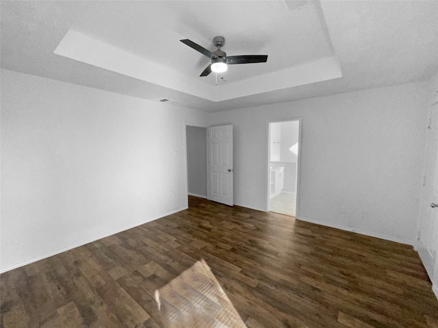 empty room featuring a tray ceiling, ceiling fan, and dark wood-type flooring