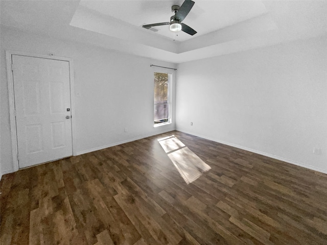 spare room featuring dark hardwood / wood-style floors, ceiling fan, and a raised ceiling