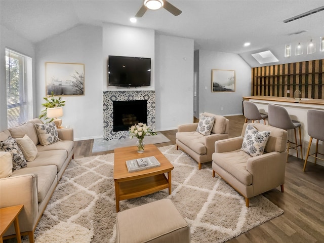 living room featuring hardwood / wood-style flooring, a fireplace, and vaulted ceiling with skylight