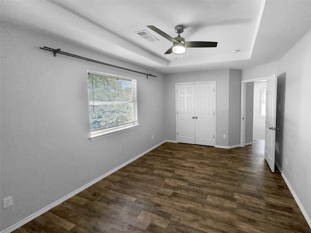 unfurnished bedroom with ceiling fan, a raised ceiling, dark wood-type flooring, and a closet