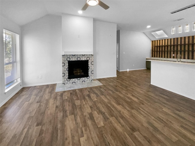 unfurnished living room with a tile fireplace, dark wood-type flooring, vaulted ceiling with skylight, and ceiling fan