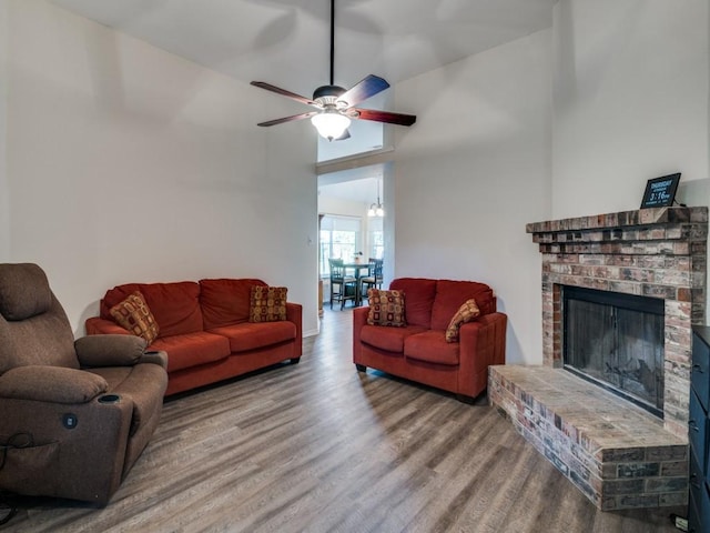 living area with a high ceiling, a brick fireplace, wood finished floors, and a ceiling fan