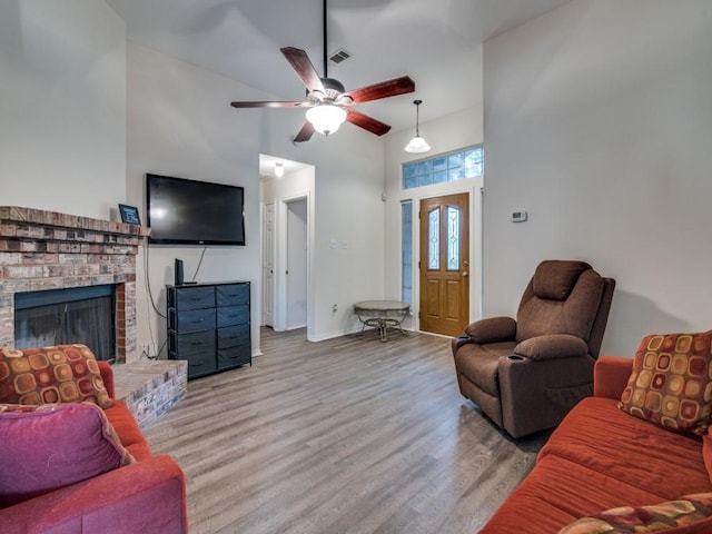 living area with a fireplace, a high ceiling, a ceiling fan, wood finished floors, and baseboards