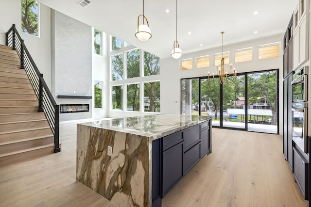 kitchen with decorative light fixtures, light hardwood / wood-style flooring, a large island, light stone counters, and a chandelier