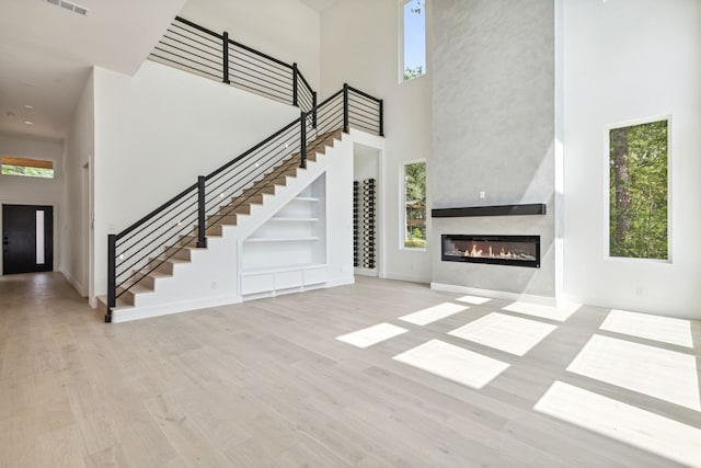 unfurnished living room with a large fireplace, a towering ceiling, and light hardwood / wood-style flooring