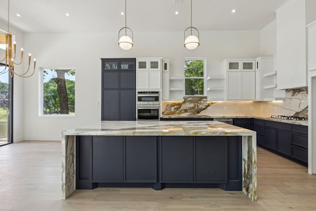 kitchen featuring light wood-type flooring, white cabinetry, hanging light fixtures, and light stone counters